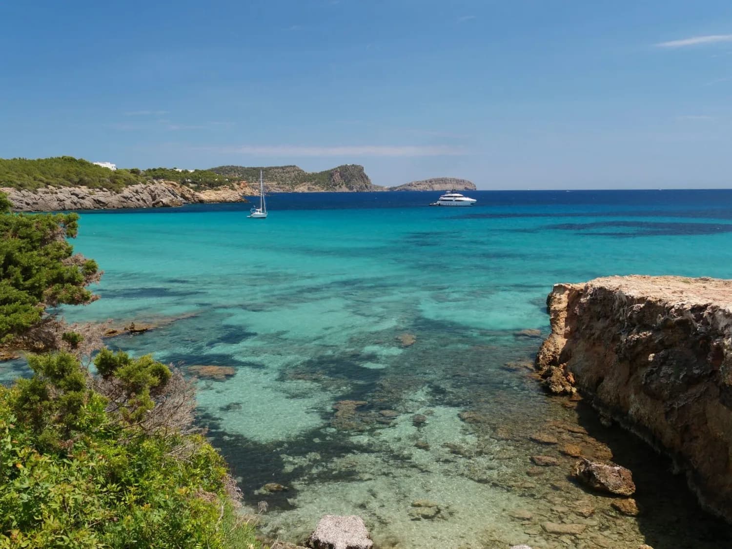 Türkisblaues Meer und felsige Küste von Ibiza mit klarem Wasser, Segelboot und Yacht in einer idyllischen Bucht