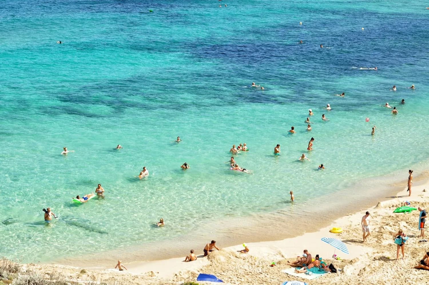 Strand auf Mallorca mit türkisblauem Meer, Badegästen im flachen Wasser und Sonnenschirmen am Sandufer