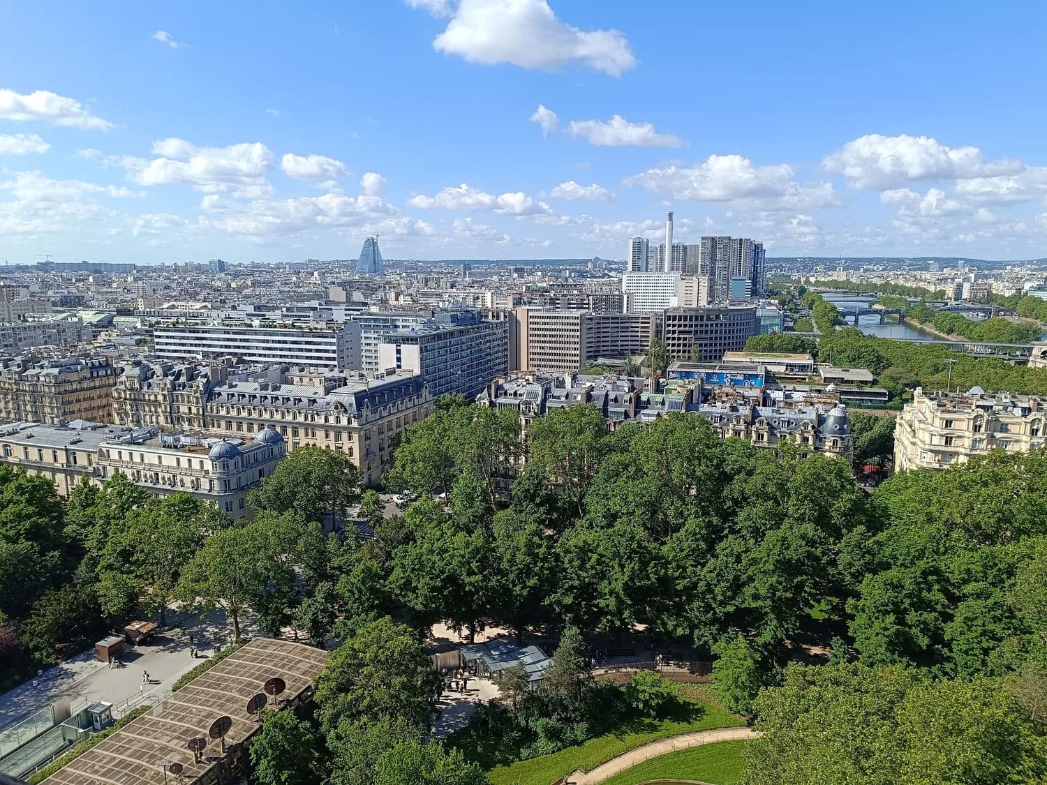 Luftaufnahme von Paris mit Baumkronen im Vordergrund, Haussmann-Häusern, moderner Uferbebauung und der Seine bei klarem Himmel