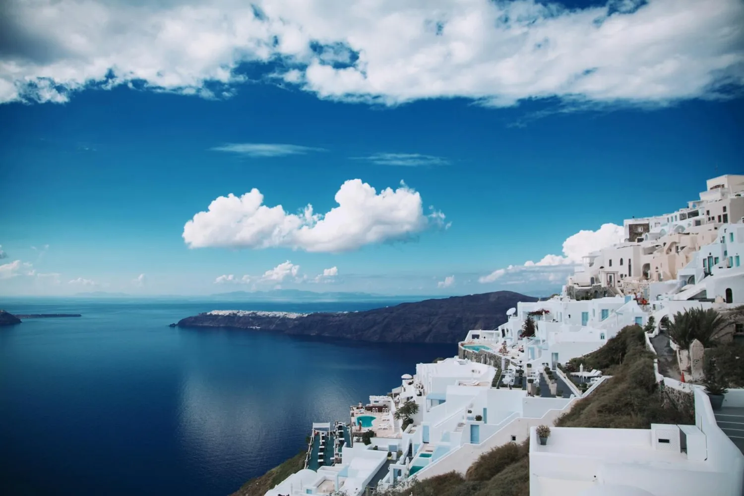 Weiße Häuser und Terrassen an der Steilküste von Santorini mit Blick auf tiefblaues Meer und wolkigen Himmel
