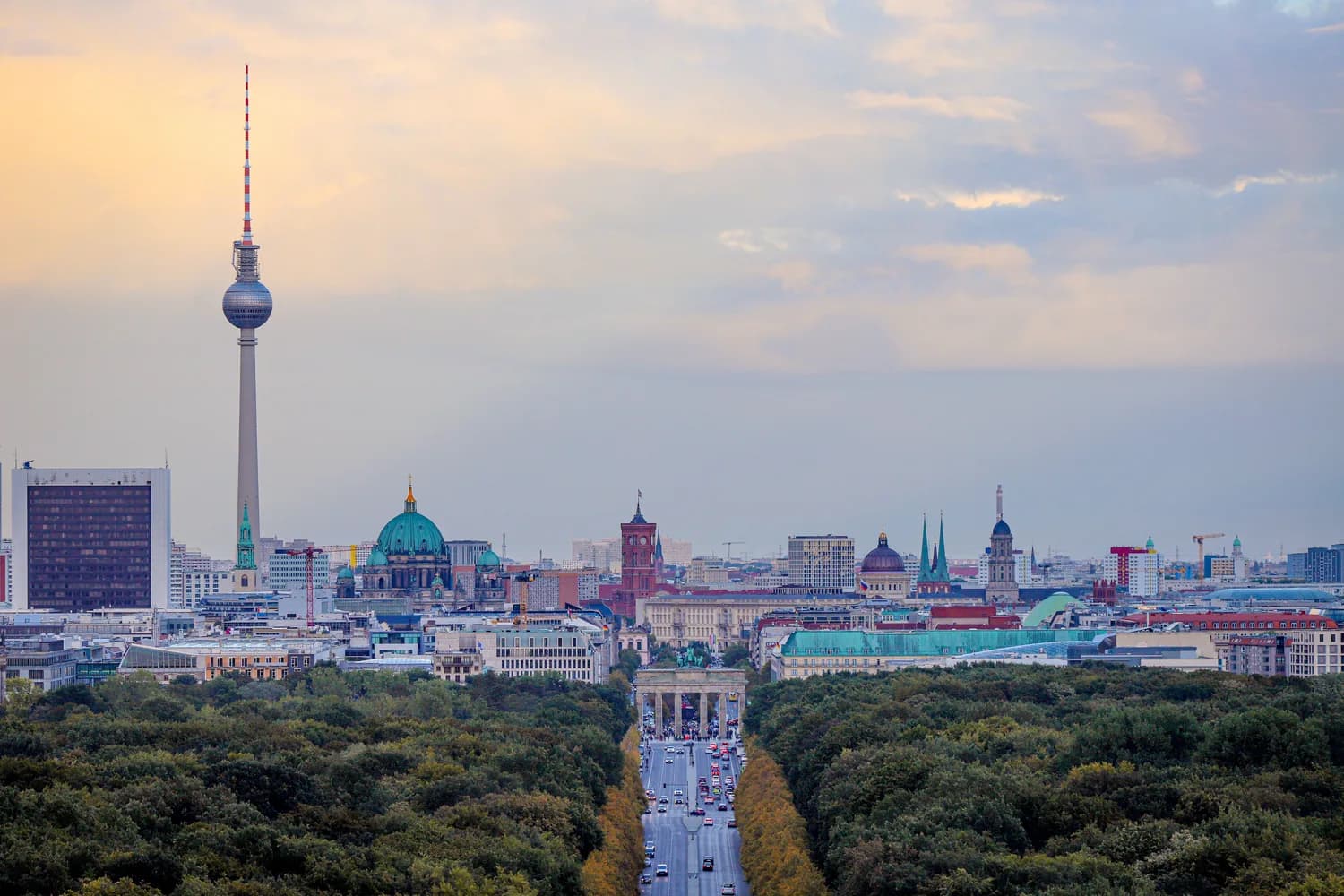 Blick auf Berliner Skyline mit Fernsehturm, Berliner Dom und Brandenburger Tor an einer Allee, städtische Dächer und Bäume im Vordergrund