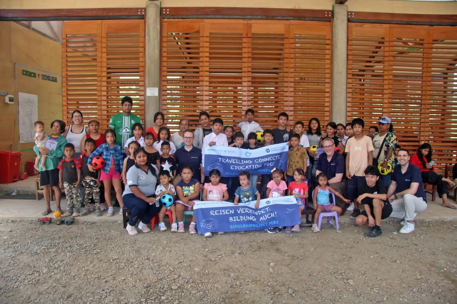 Gruppenfoto von Kindern, Lehrern und Freiwilligen bei einem Schulbauprojekt in Peru mit Bannern, Fußbällen und Schulmaterialien im Schulgebäude