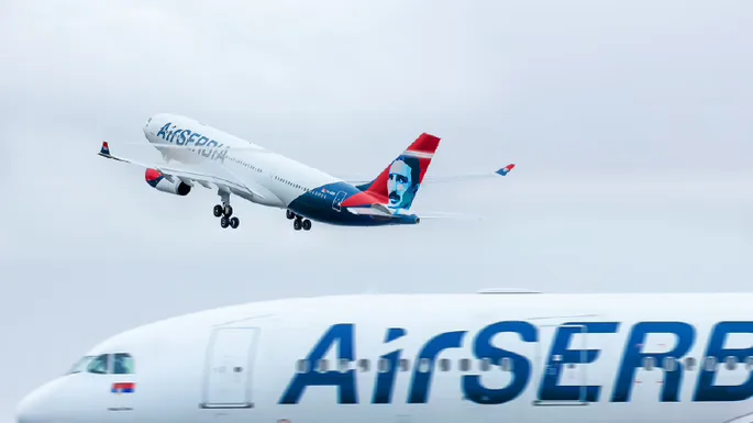 AirSerbia Airbus A330 im Steigflug über einem am Boden stehenden AirSerbia Flugzeug mit markanter Heckbemalung und Airline-Logo