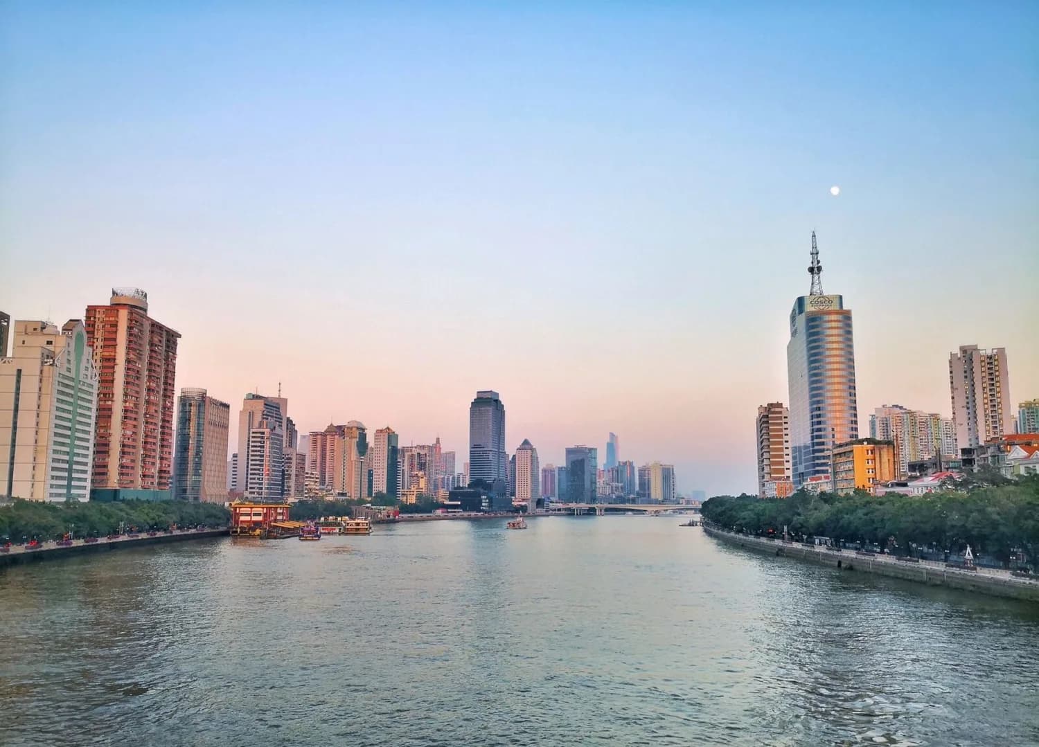 Panoramablick auf Guangzhou Skyline am Fluss mit Hochhäusern, Uferpromenade und Booten bei sanfter Abenddämmerung