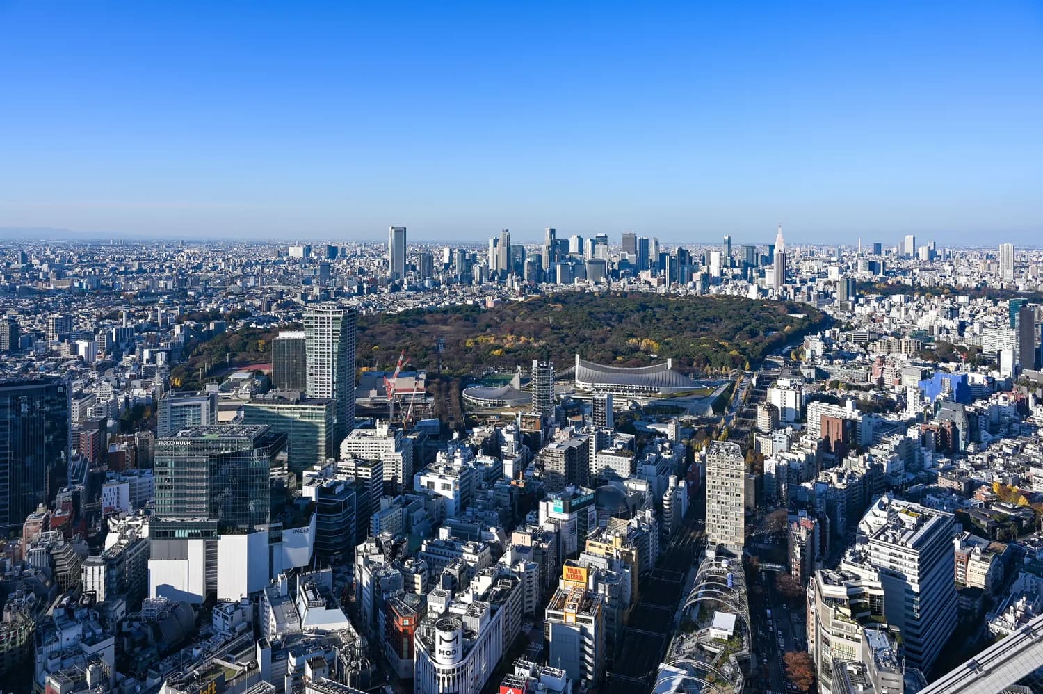 Luftaufnahme von Tokios Shinjuku mit großem Park, Stadion und moderner Skyline bei klarem Himmel