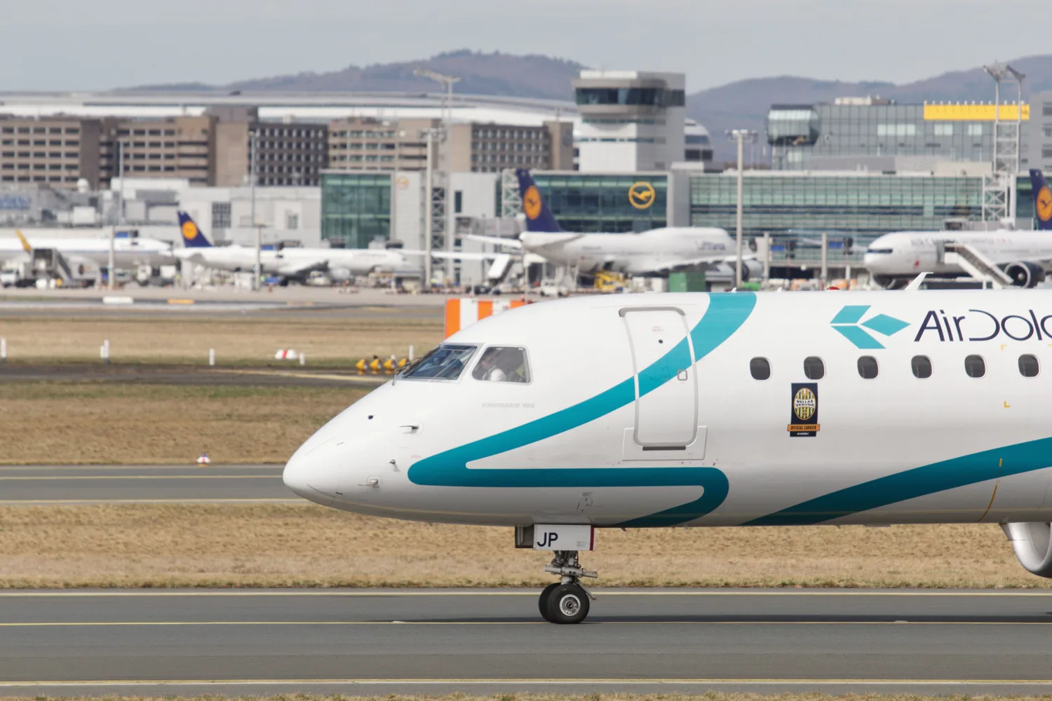 Regionaljet von Air Dolomiti auf dem Rollfeld vor der Skyline des Frankfurter Flughafenterminals mit weiteren Flugzeugen im Hintergrund