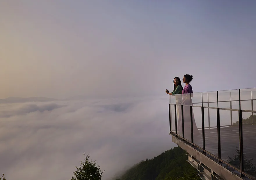 Zwei Personen auf einer Unkai-Terrasse über dem Wolkenmeer bei Sonnenaufgang, Glasgeländer und Aussichtspunkt über nebelverhangenen Bergen ©Hoshino Resorts Inc.