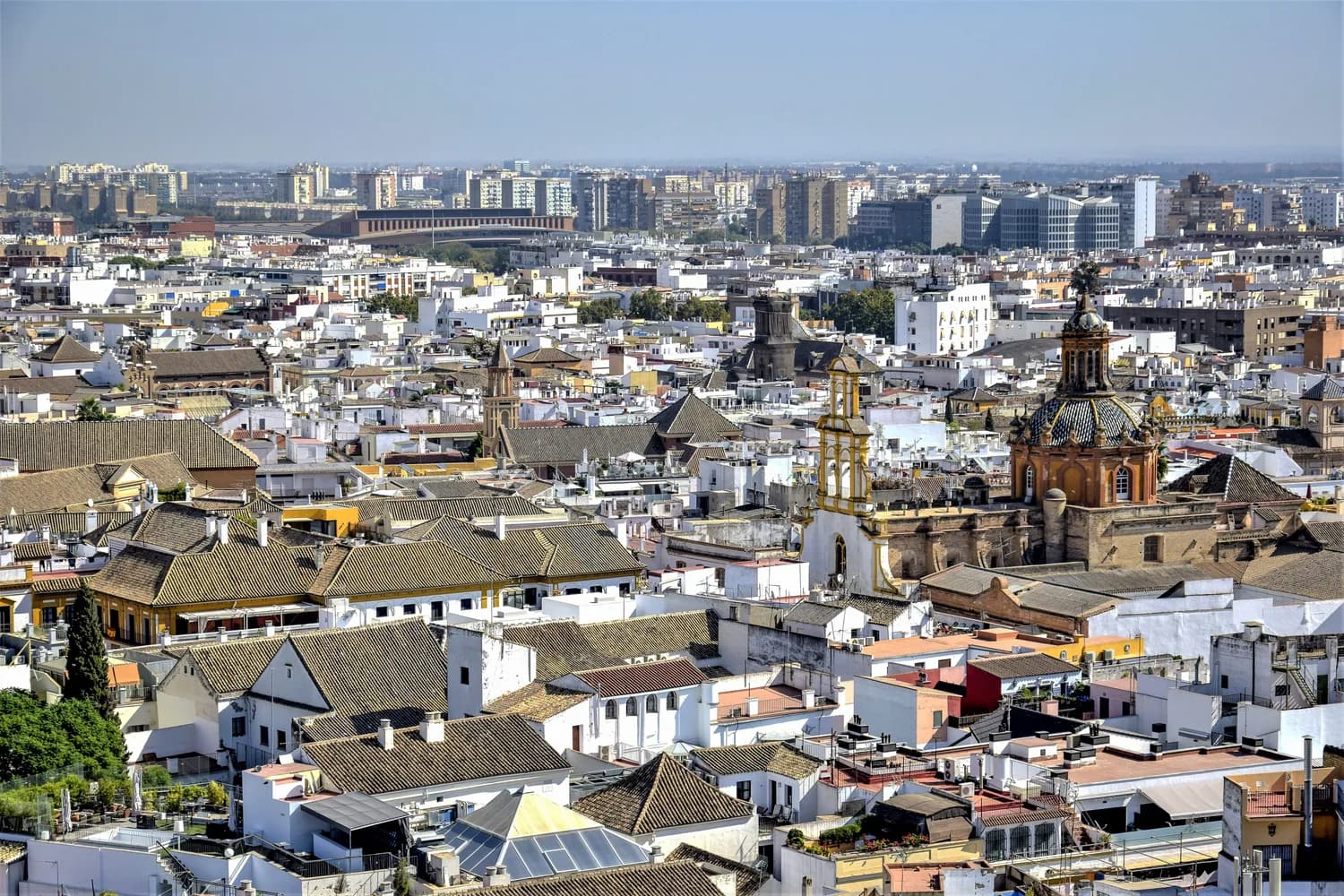 Luftaufnahme der Altstadt von Sevilla mit dicht stehenden weißen Häusern, historischen Kirchenkuppeln und traditioneller andalusischer Architektur