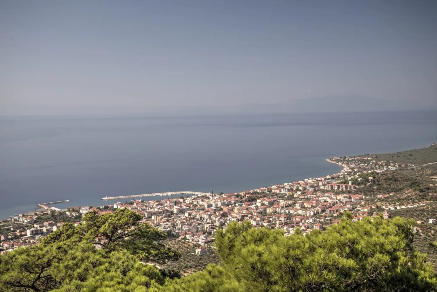 Panoramablick auf die Küstenstadt Edremit und den Golf von Edremit in der Türkei mit Hafen, Strandpromenade und bewaldeten Hügeln im Vordergrund