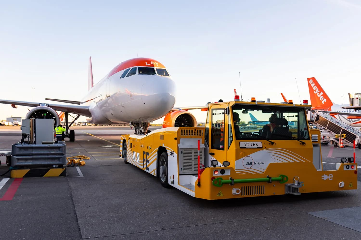 Elektrische Taxibot zieht easyJet Passagierflugzeug am Flughafen, Bodenpersonal und Terminalausrüstung im Vordergrund