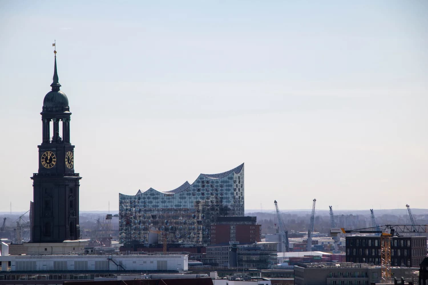 Hamburg Skyline mit St. Michaelis Turm im Vordergrund und der gläsernen Elbphilharmonie an der Elbe, urbanes Hafenpanorama und Kräne im Hintergrund