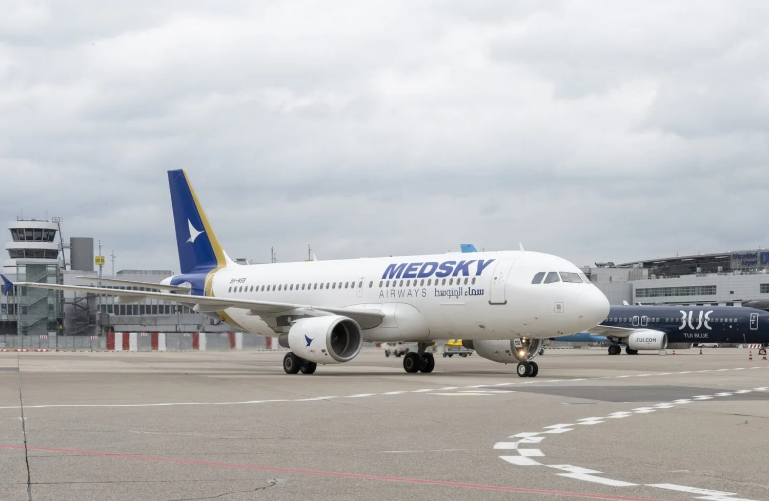 MedSky Airways A320 am Rollfeld eines Flughafens, parkend vor Terminals und Tower