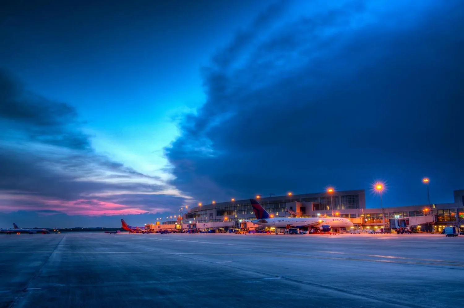 Flughafen-Terminal bei Dämmerung mit geparkten Passagierflugzeugen am Gate, beleuchtetes Vorfeld und dramatischer blauer Himmel (c) Bild flyaustin.com