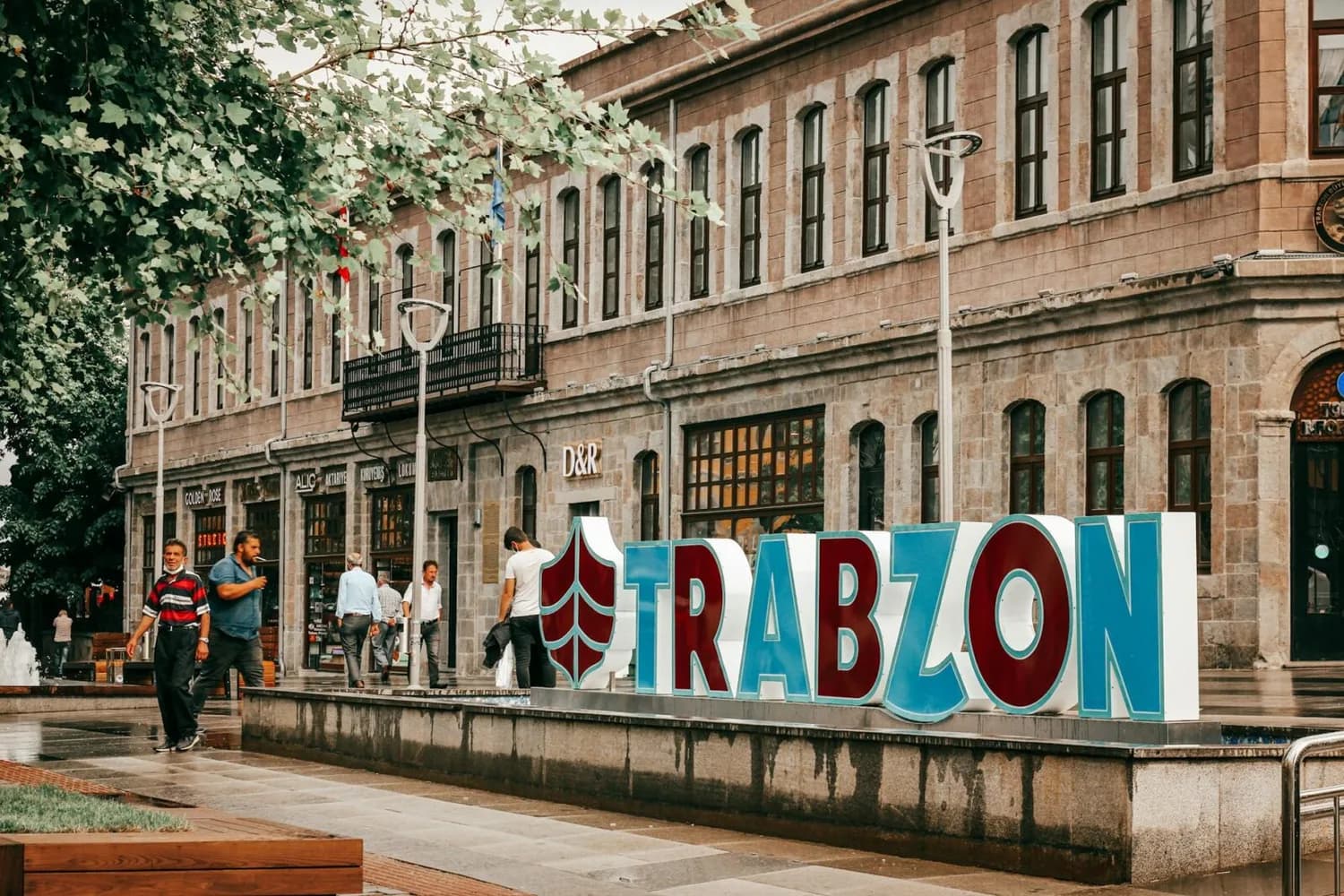 Große bunte TRABZON Buchstaben vor historischem Steingebäude mit Passanten auf belebtem Platz in Trabzon, Türkei