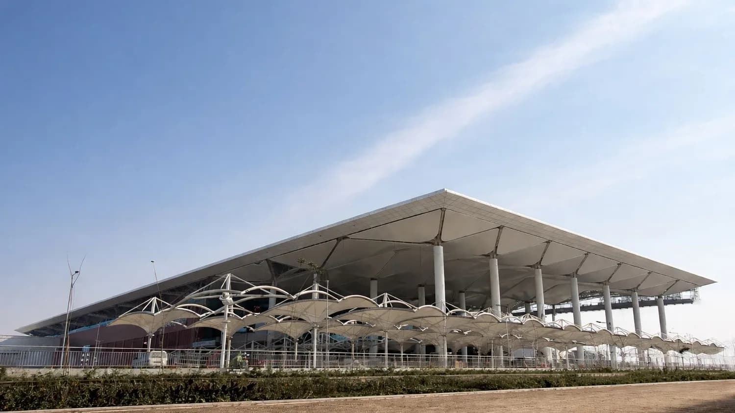Noida International Airport Terminal mit modernem wellenförmigem Vordach, Säulenhalle und überdachtem Vorfahrtsbereich bei klarem Himmel