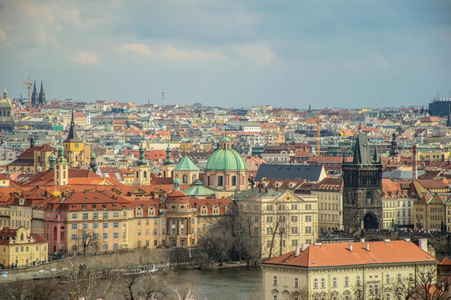 Panoramablick auf Prager Altstadt mit roten Dächern, grüner Kuppel der St.-Nikolaus-Kirche, gotischem Pulverturm und Moldauufer bei klarem Himmel