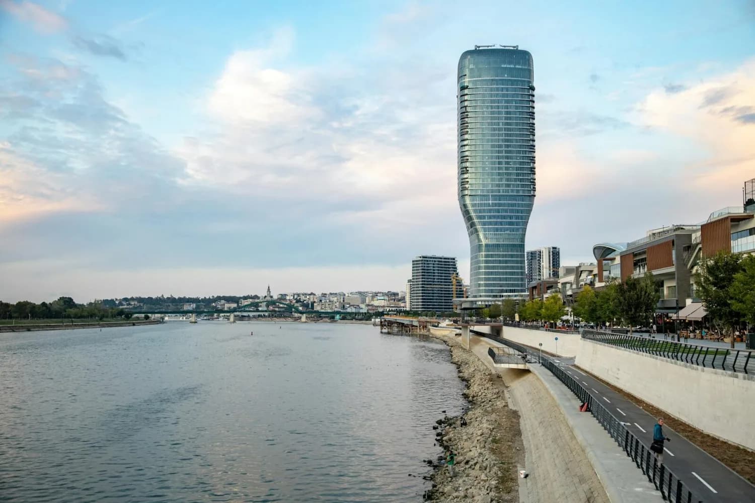 Panorama der Donauuferpromenade mit modernem Hochhaus und Uferweg, Stadtansicht Belgrad im Sommerflugplan von Köln Bonn