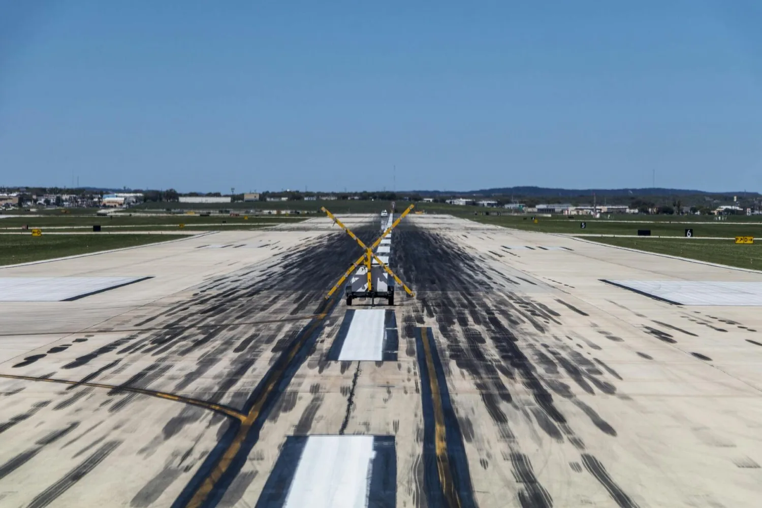 gesperrte Landebahn mit gelbem Absperrkreuz, Start- und Landemarkierungen und Spurrillen auf Betonfläche am Flughafen