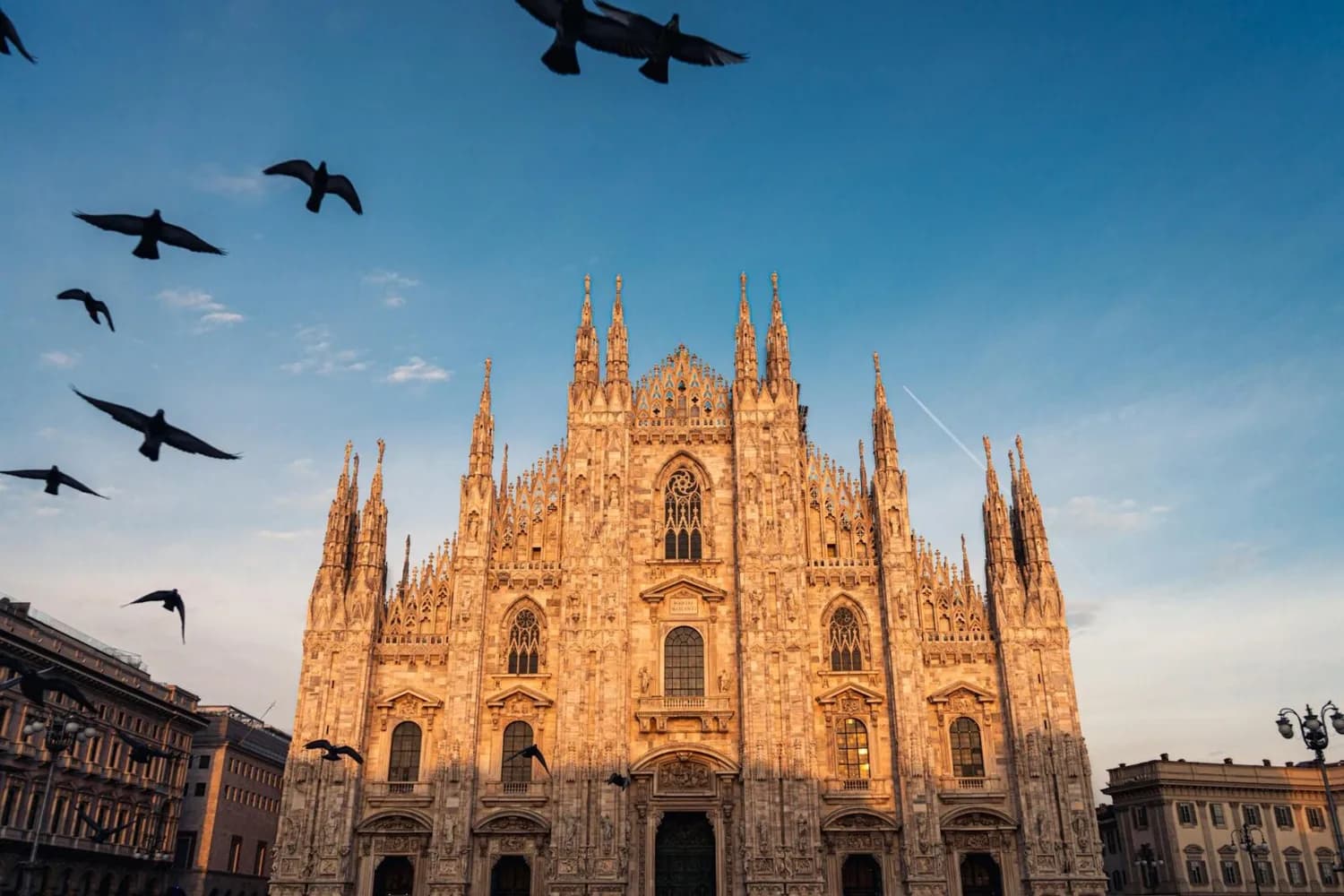 Mailänder Domfassade bei Sonnenuntergang mit fliegenden Tauben und blauem Himmel