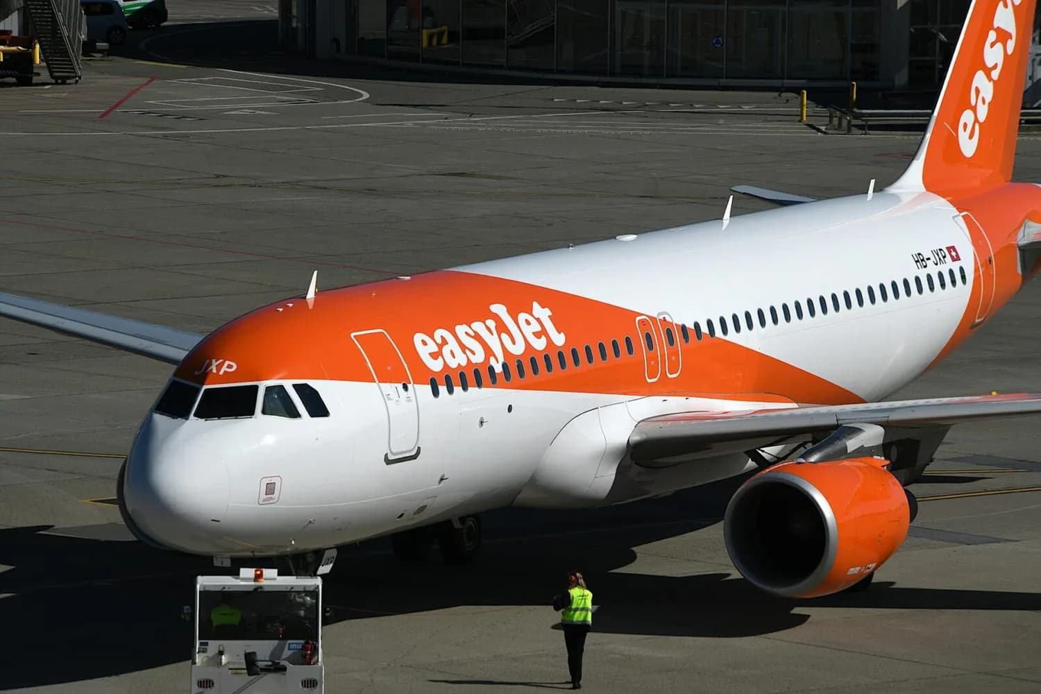 EasyJet Passagierflugzeug mit orange-weißem Rumpf am Flughafenvorfeld, Bodenpersonal neben Bugfahrwerk