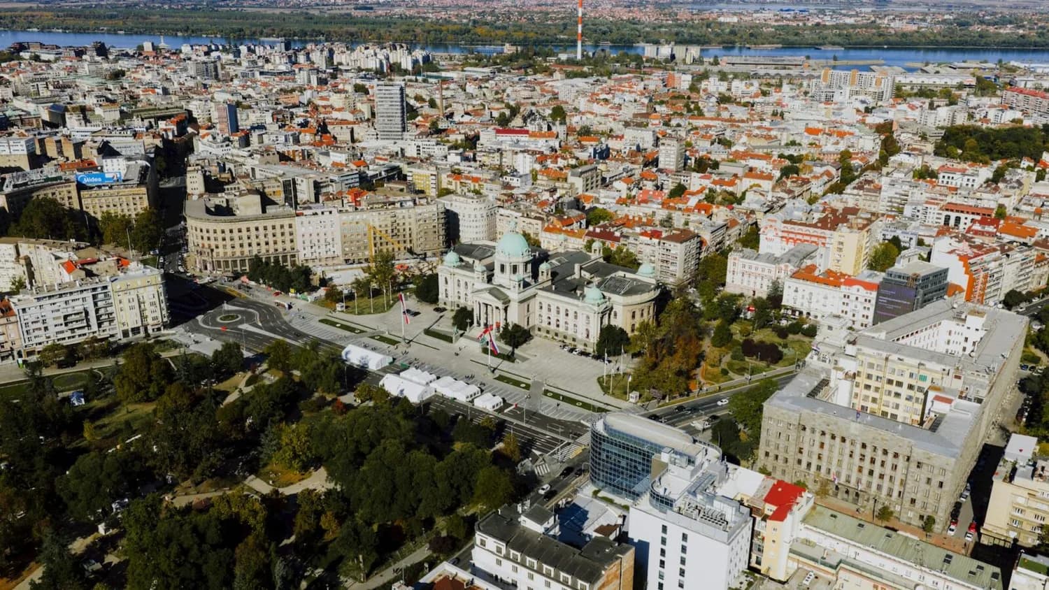 Luftaufnahme von Belgrad mit Nationalversammlung, weitläufigem Platz, umliegenden Wohn- und Verwaltungsgebäuden und Donau im Hintergrund