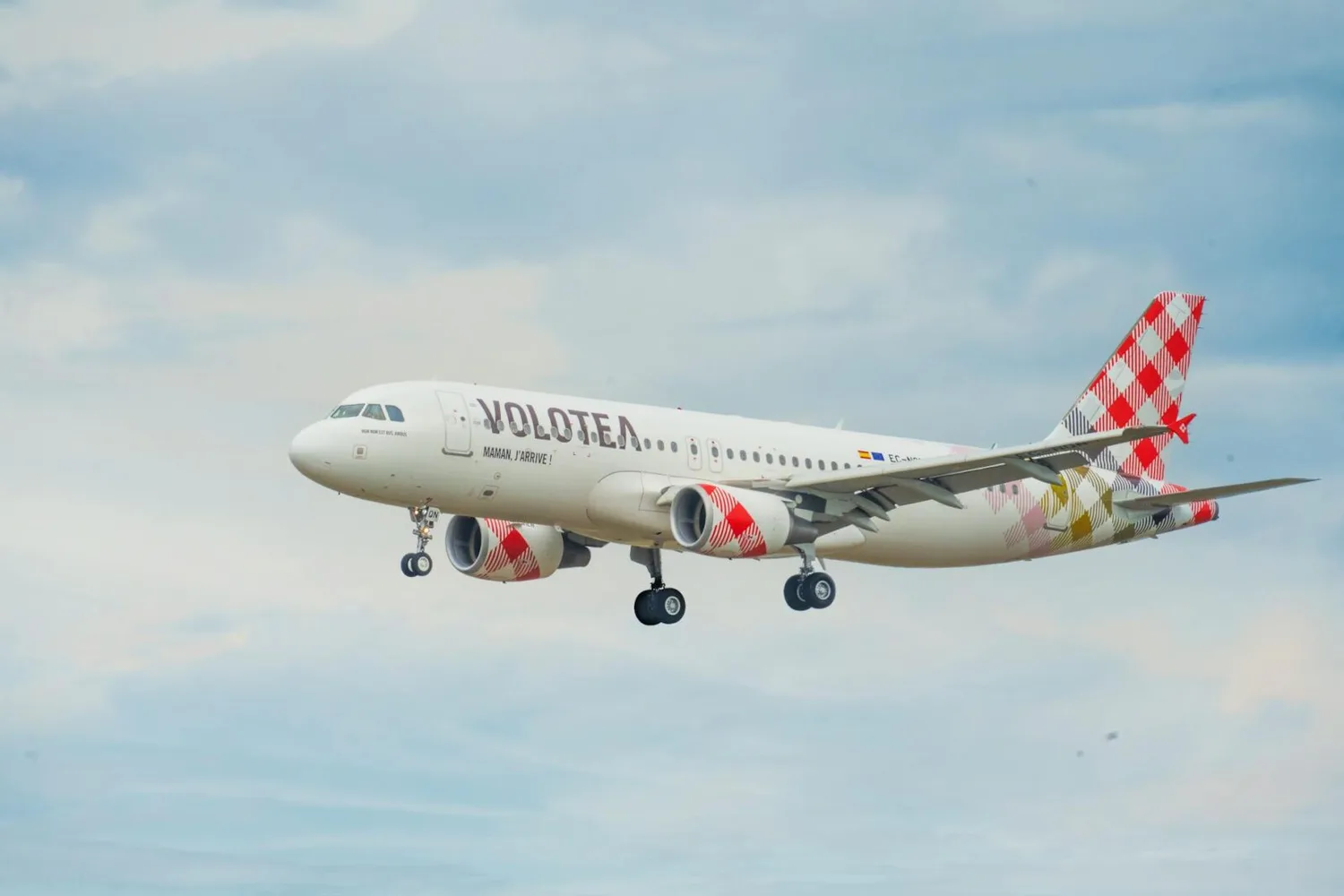 Volotea Passagierflugzeug im Landeanflug mit ausgefahrenem Fahrwerk und markanter rot-weiß karierter Heckbemalung