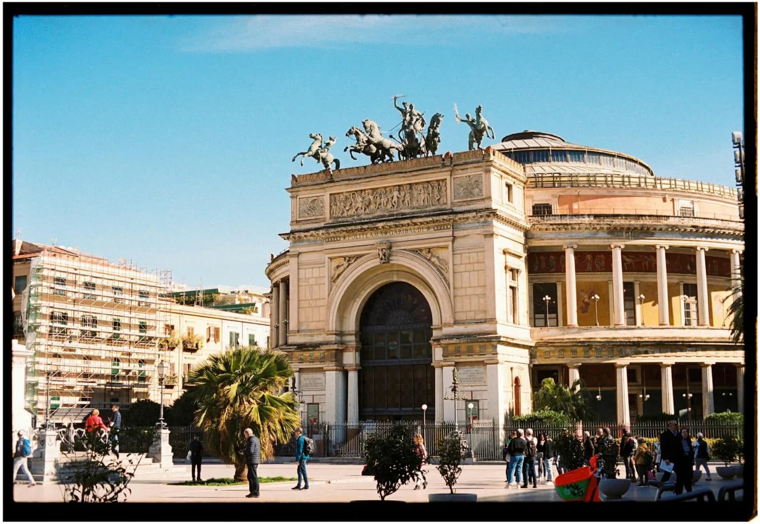Teatro Politeama Garibaldi in Palermo mit klassischer Fassade, Quadriga-Skulpturen auf dem Dach, Palmen und Passanten auf dem Platz in Sizilien