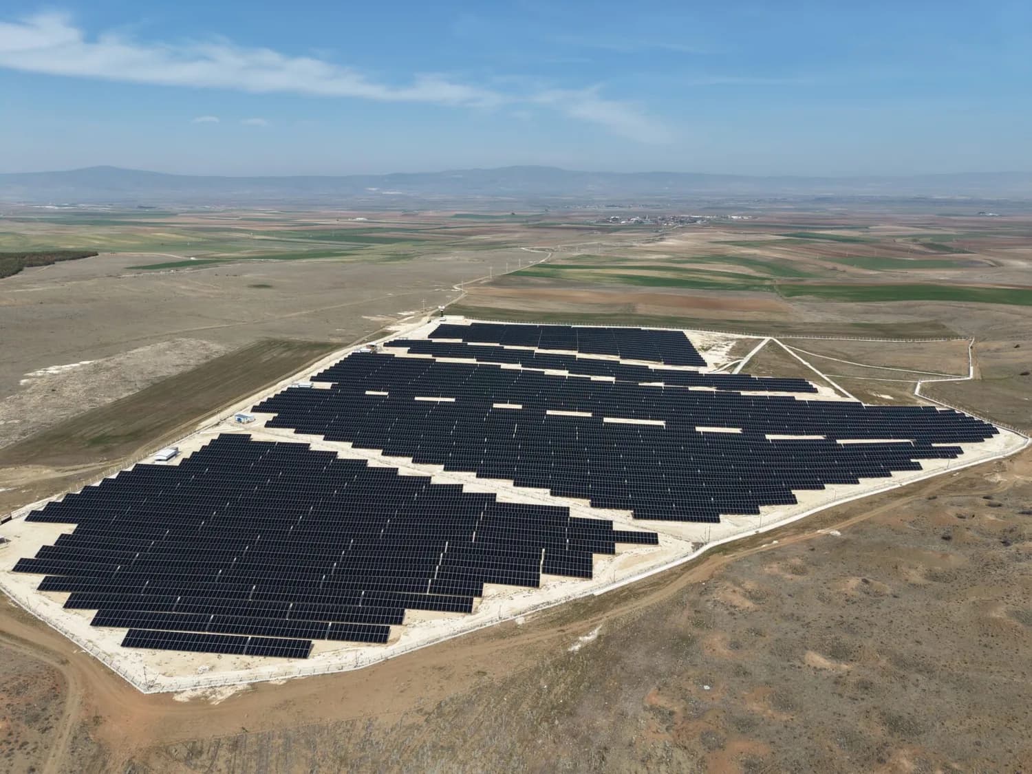 Luftaufnahme großer CVK SolarSystem Photovoltaik-Freiflächenanlage auf karger Landschaft mit Reihen dunkler Solarmodule und weiter Agrarlandschaft im Hintergrund