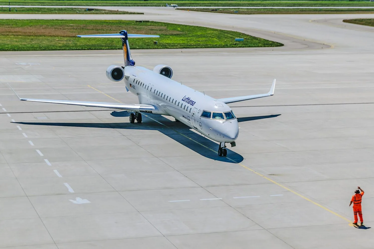 Lufthansa Regional Jet auf Rollfeld mit Tankwart in orangener Sicherheitskleidung beim Ground Handling