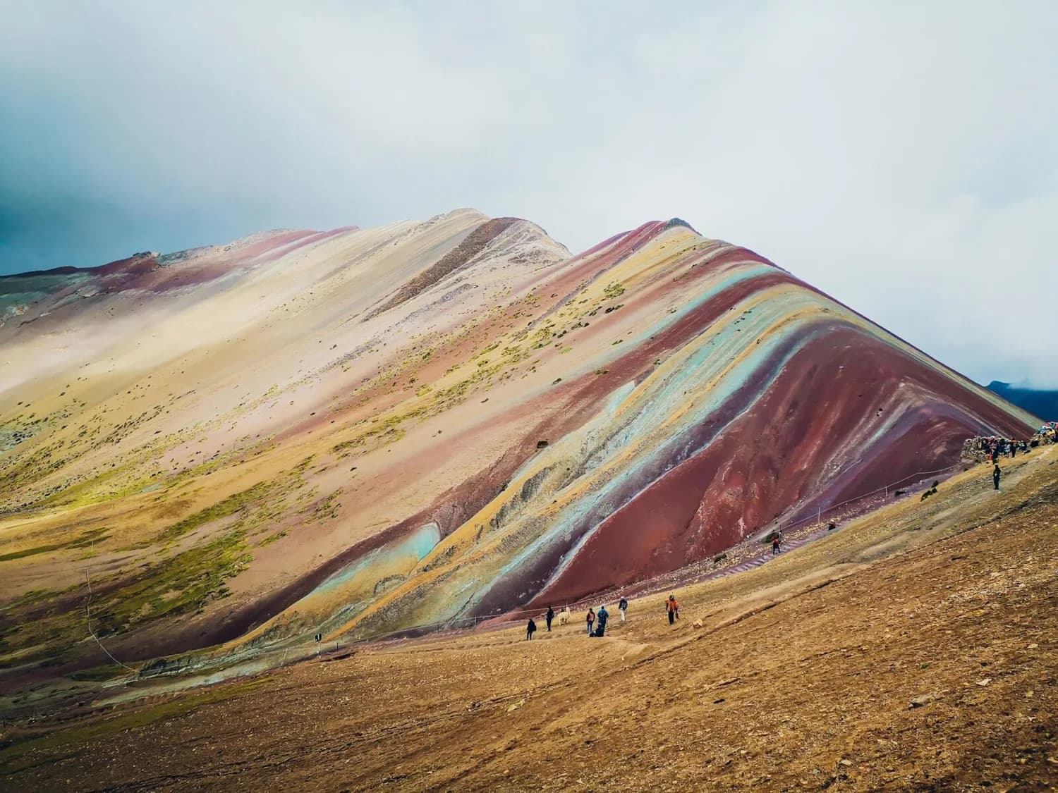 Bunte, gestreifte Berge von Vinicunca (Rainbow Mountain) in Peru mit Wanderern am Fuß und wolkigem Himmel