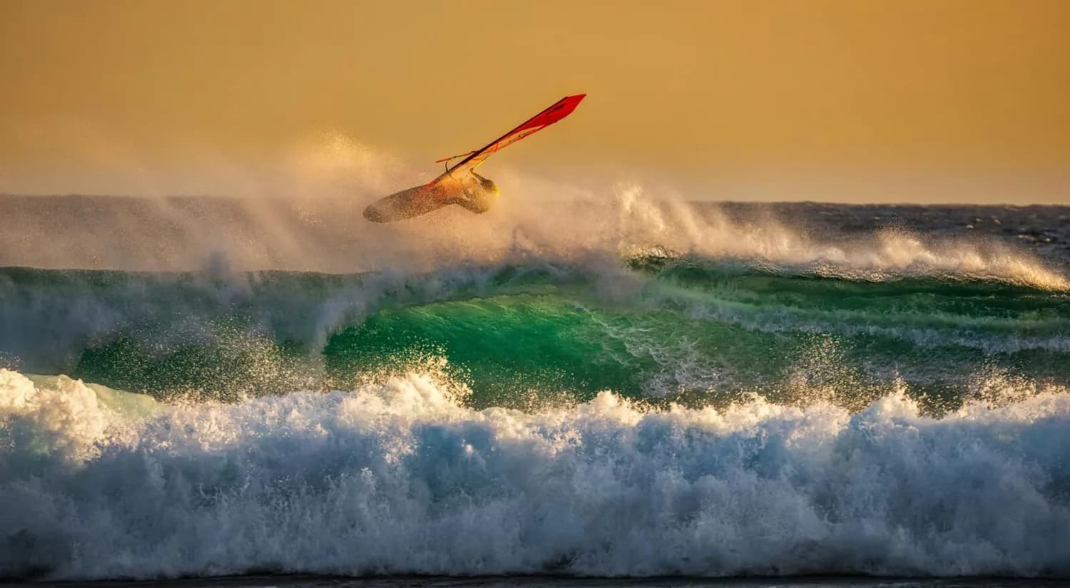 Windsurfer springt über große grüne Welle bei Sonnenuntergang, actionreiches Surfen als Reisemotiv Kreta Bremen Zielstrand