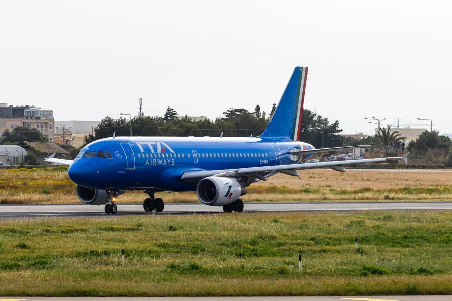 ITA Airways Passagierflugzeug in blauer Lackierung beim Rollen auf dem Flughafenvorfeld mit sichtbarem Leitwerk und Triebwerken