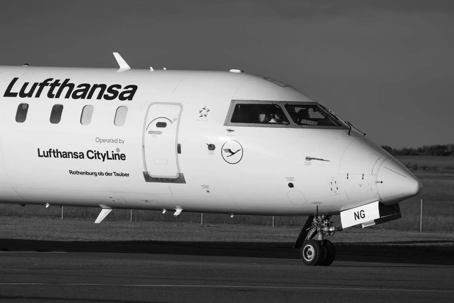 Lufthansa CityLine Regionaljet beim Rollen am Flughafen, Nahaufnahme Cockpit‑Fenster, Passagiertür und Bugfahrwerk mit Airline‑Branding