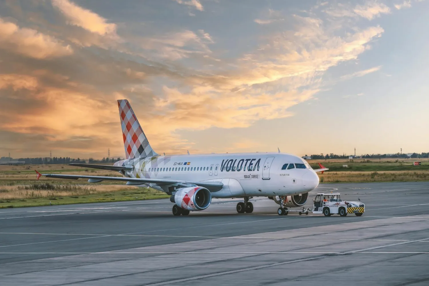 Volotea Passagierflugzeug auf Rollfeld bei Sonnenuntergang, Flugzeug mit gemusterter Heckflosse und Bodenfahrzeug am Bug