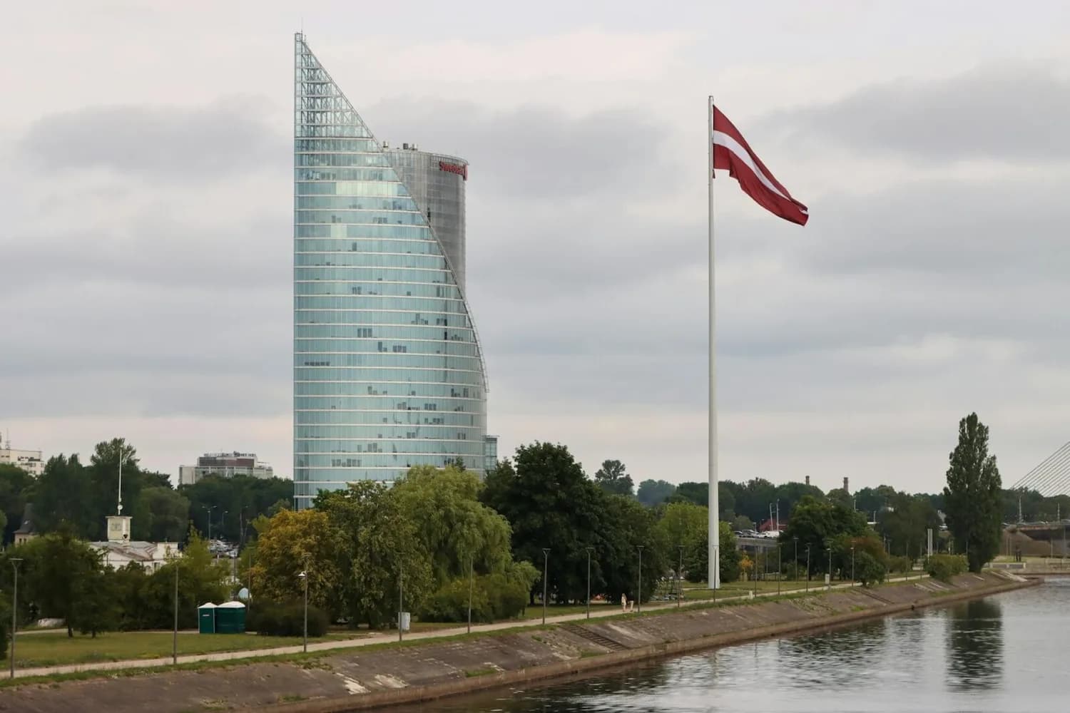 Moderner Glasbüroturm an der Daugava mit großer lettischer Flagge und Uferpromenade in Riga