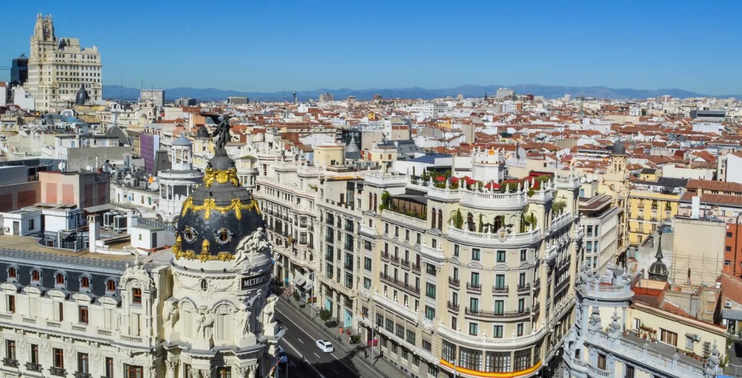 Blick über Madrids Gran Vía mit der markanten Metropolis-Kuppel, historischen Fassaden, Dachterrassen und Stadtpanorama bei klarem Himmel