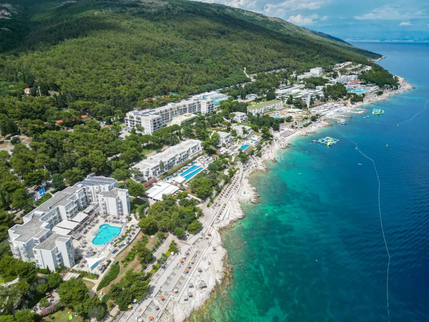 Luftaufnahme der kroatischen Küste mit Hotels, Pools, felsigen Stränden und klarem türkisblauem Meer