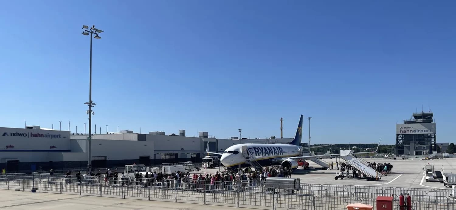 Passagiere beim Einsteigen in eine Ryanair-Maschine auf dem Vorfeld des Flughafens Hahn mit Terminal und Tower im Hintergrund