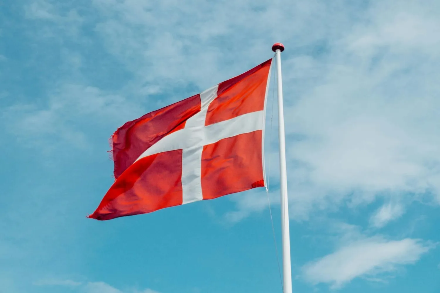 Dänische Flagge (Dannebrog) mit weißem Kreuz auf rotem Feld weht an Fahnenmast vor blauem Himmel
