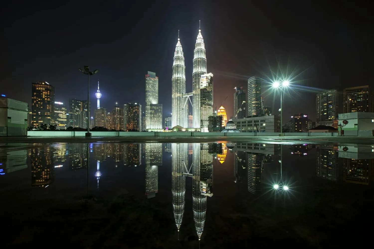 Nachtaufnahme der beleuchteten Petronas Twin Towers und Skyline von Kuala Lumpur mit Spiegelung in einer Wasserfläche, urbanes Stadtbild, Direktverbindung Bergamo Kuwait Hinweis: Flugverbindung Thema