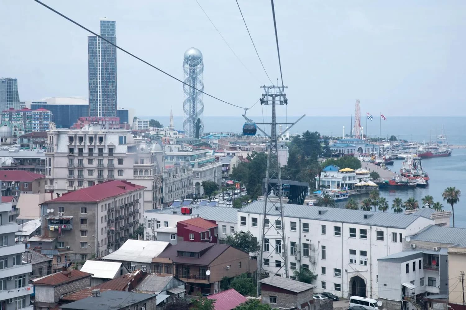 Blick auf Batumi Georgien mit Seilbahn über der Stadt, moderner Alphabet Tower, Hafenpromenade, Fähren und Freizeitpark am Schwarzen Meer, urbane Wohngebäude im Vordergrund