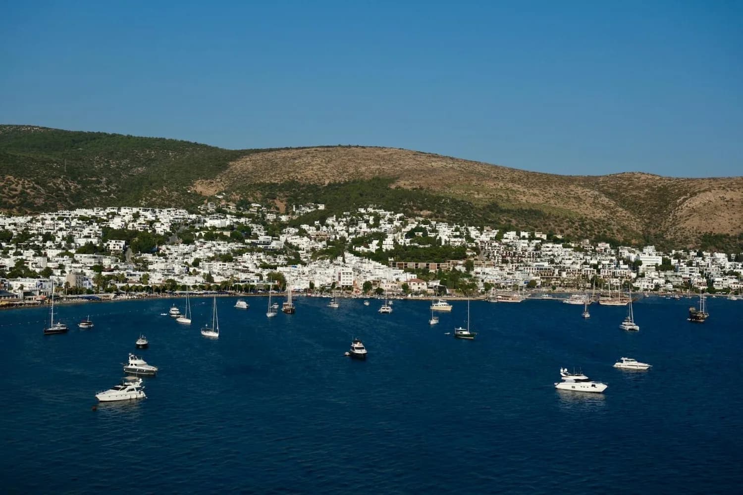 Bodrum Küste mit weiß getünchten Häusern am Hang, blauem Meer und mehreren Segel- und Motorbooten im Hafen