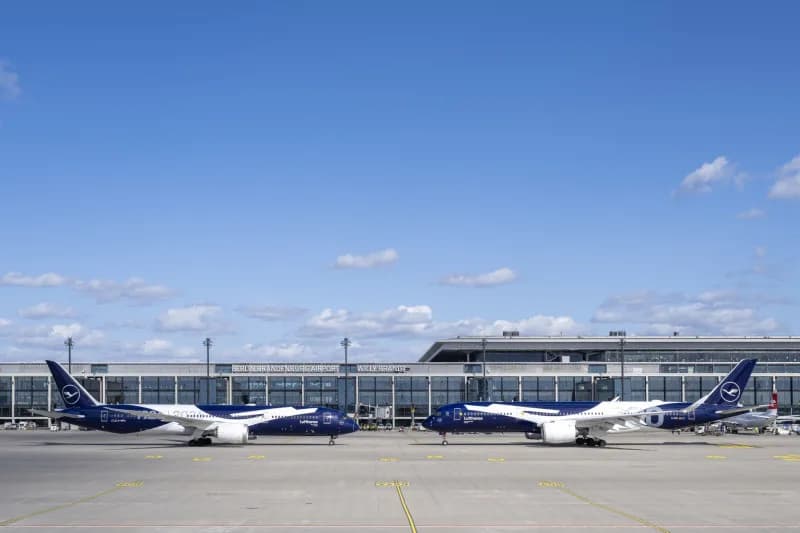 Zwei Lufthansa Flugzeuge mit dunkelblauer Sonderlackierung stehen nebeneinander am Terminal eines Flughafens bei klarem Himmel