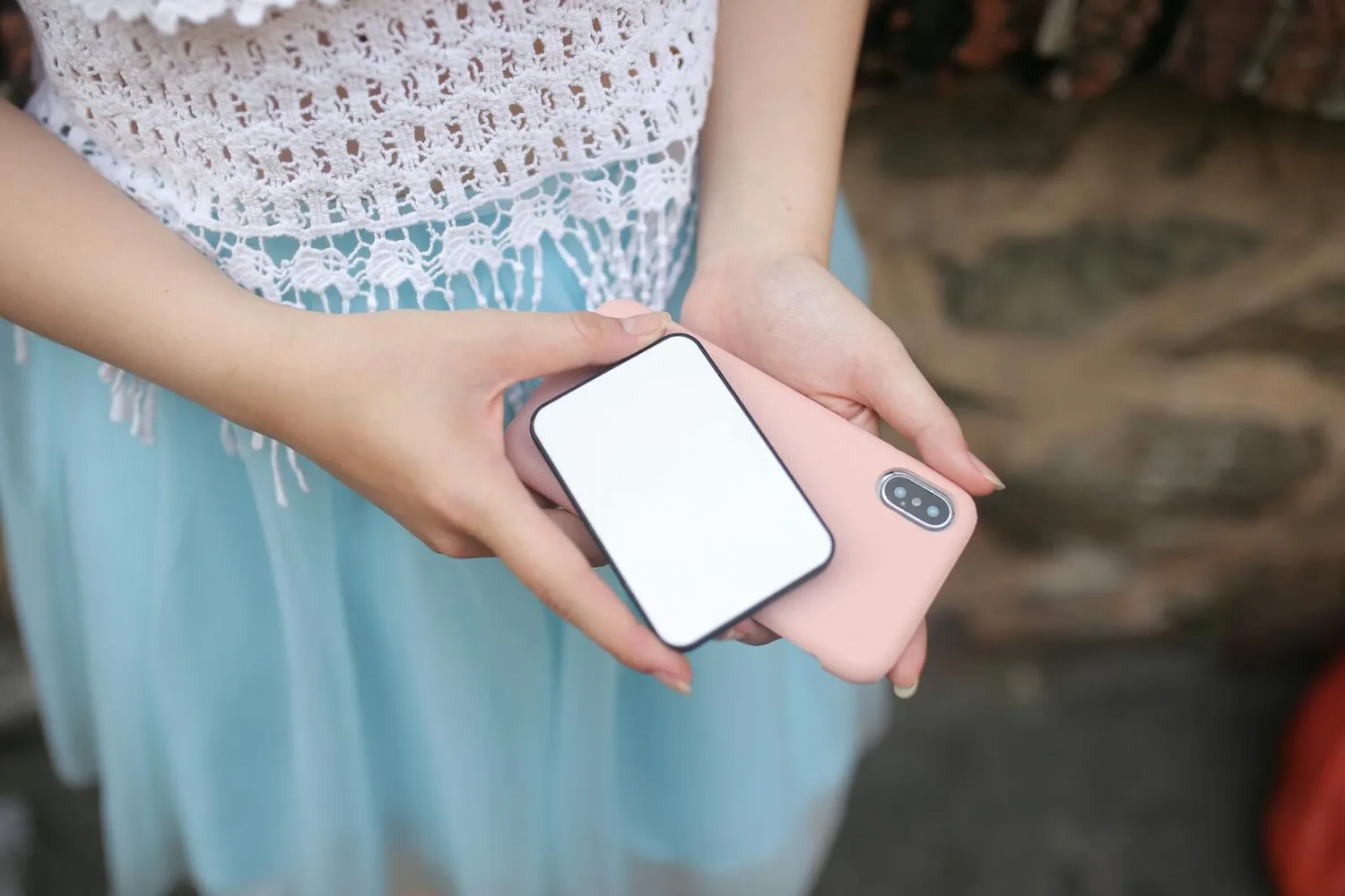 Person hält Smartphone mit rosa Hülle und tragbare Powerbank in den Händen, Nahaufnahme, Outdoor-Szene