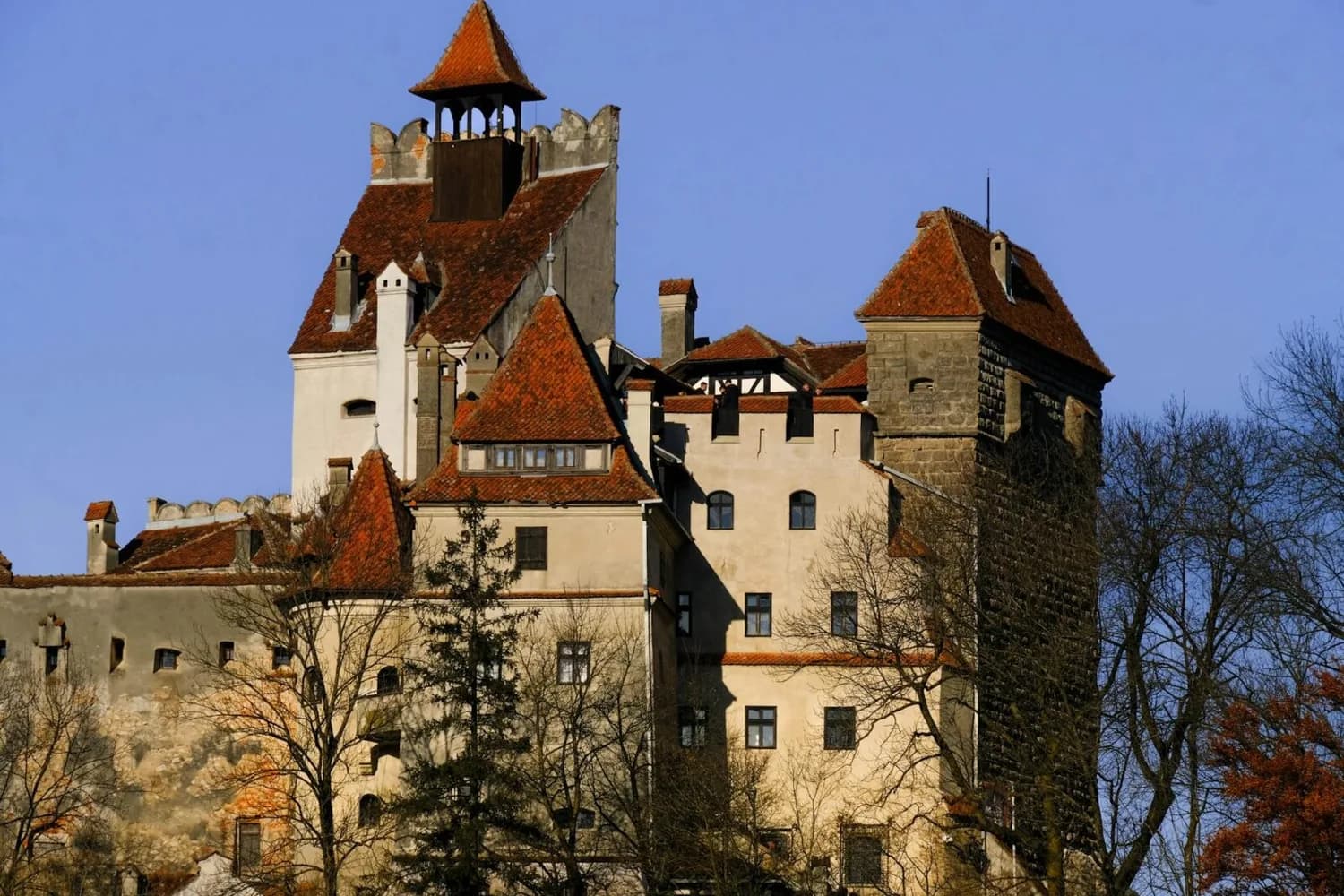 Burg Bran in Rumänien mit roten Ziegeldächern, Wehrtürmen und mittelalterlicher Fassadenansicht, umgeben von kahlen Bäumen