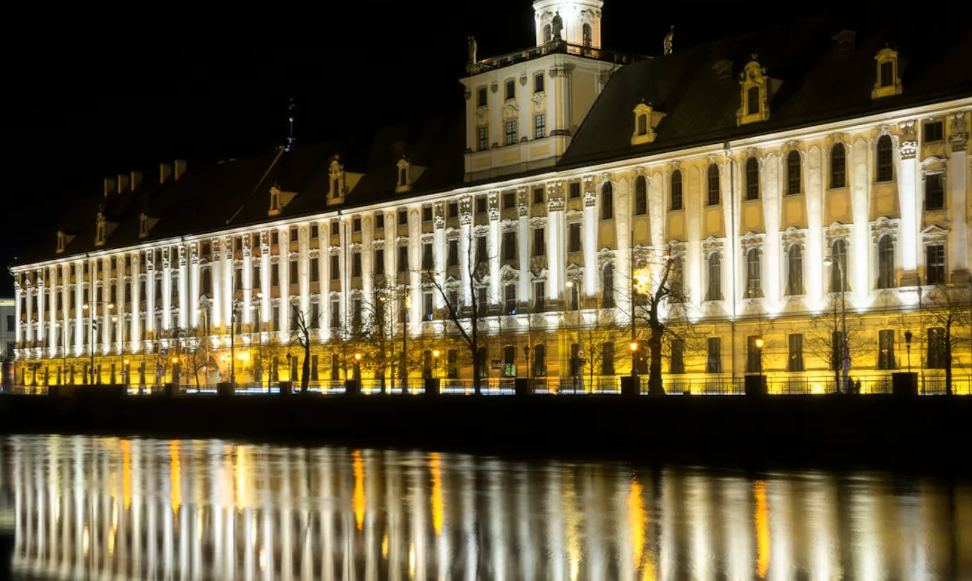 Beleuchtetes historisches Gebäude an der Oder in Breslau bei Nacht, Lichterreflexionen im Wasser, Szene erinnert an Flughafenroute Dortmund–Wrocław mit Wizz Air