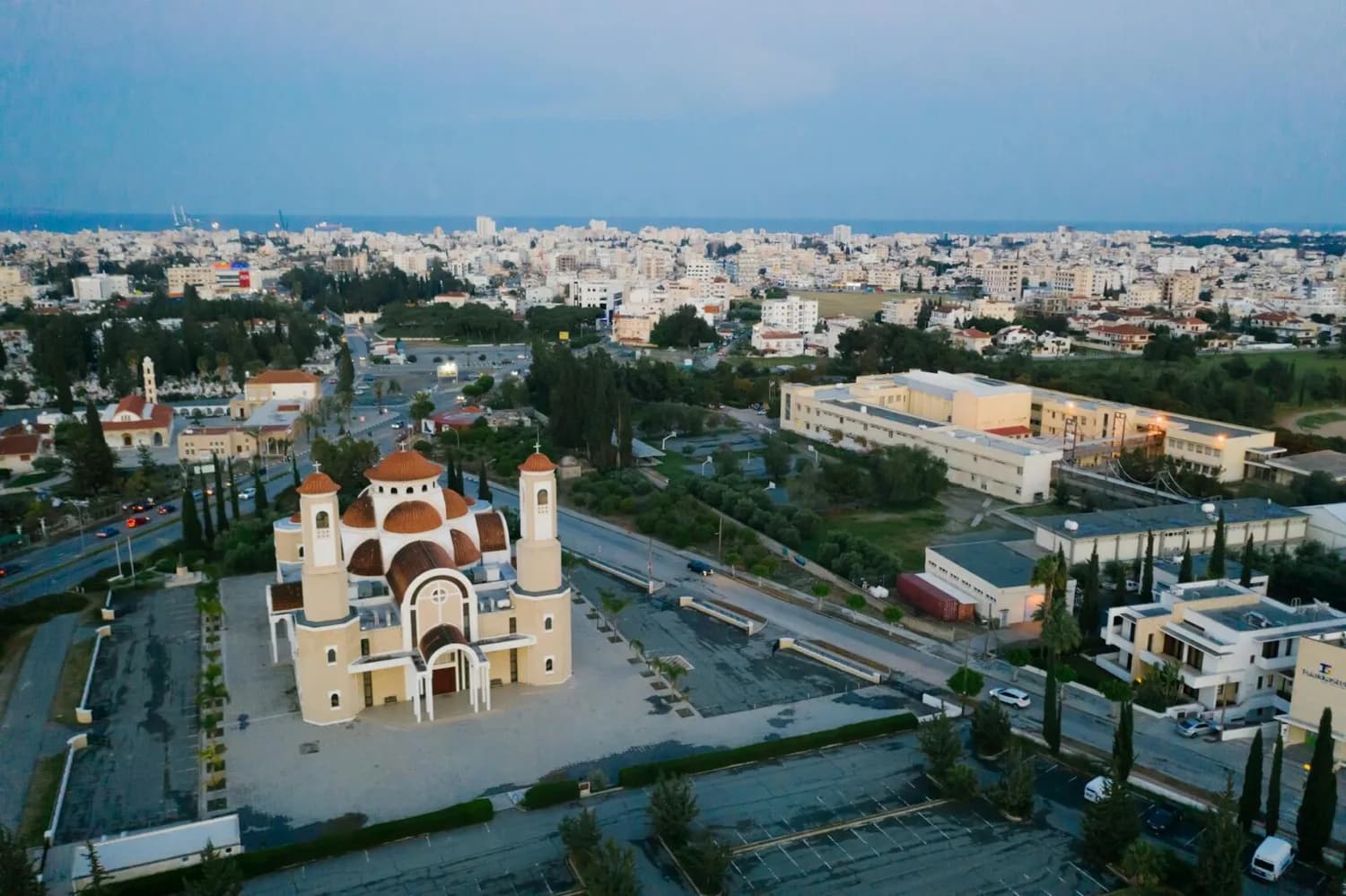 Luftaufnahme einer orthodoxen Kirche mit roten Kuppeln und Glockenturm in Larnaca, Zypern, vor städtischer Wohn- und Parkanlage am Meer