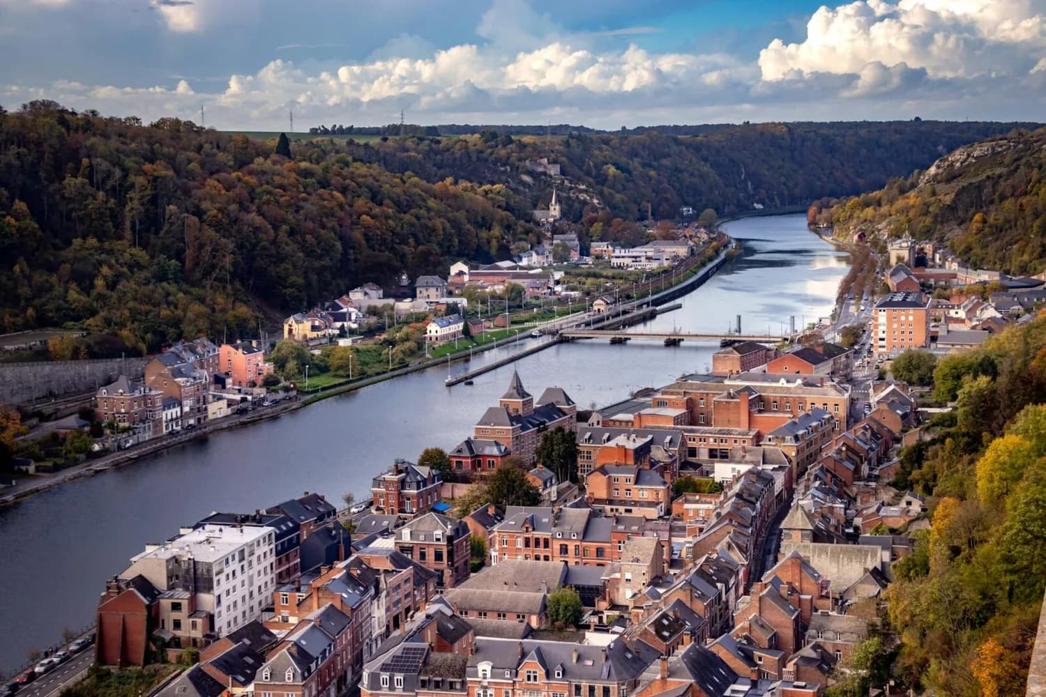 Stadtansicht an der Maas in Wallonien im Frühling, Flussufer, Brücke, rote Backsteinhäuser und bewaldete Hügel