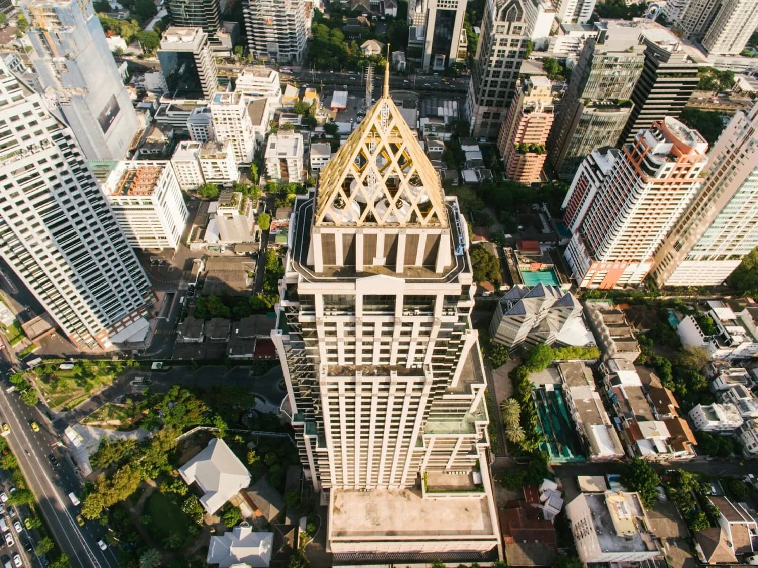 Luftaufnahme eines markanten Hochhauses mit goldener Spitze im Geschäftsviertel von Bangkok, umgeben von Bürogebäuden und grünen Innenhöfen
