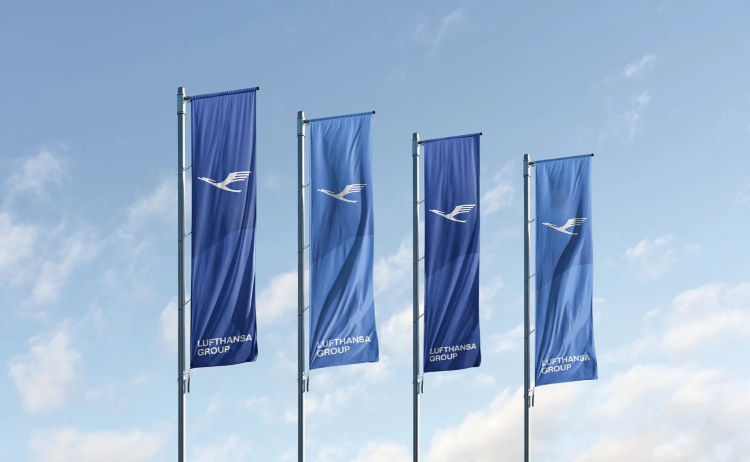 Vier blaue Fahnen mit Lufthansa Group Logo an Fahnenmasten vor blauem Himmel